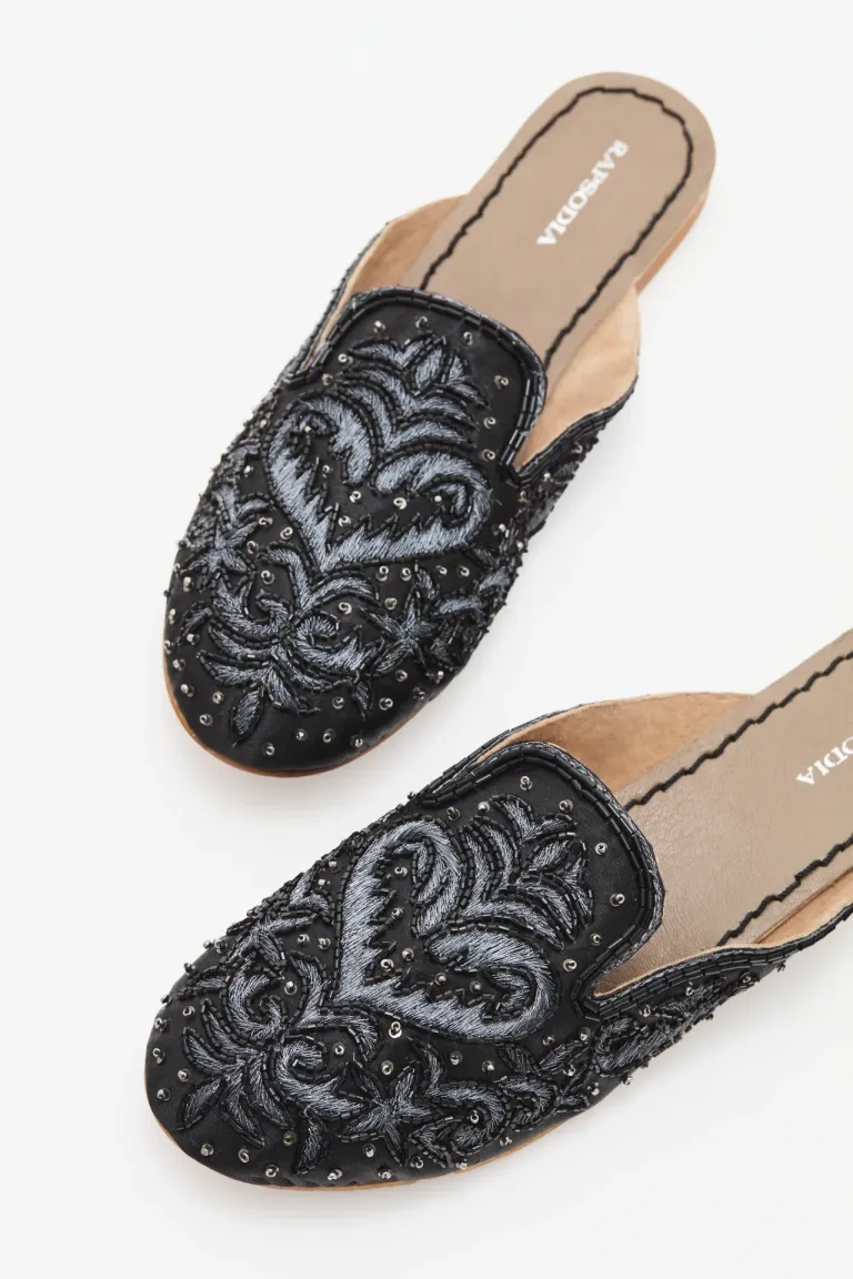 Zuecos negros con bordado decorativo en tonos plateados para un look sofisticado y femenino de Rapsodia en Zuecos Planos para argentina